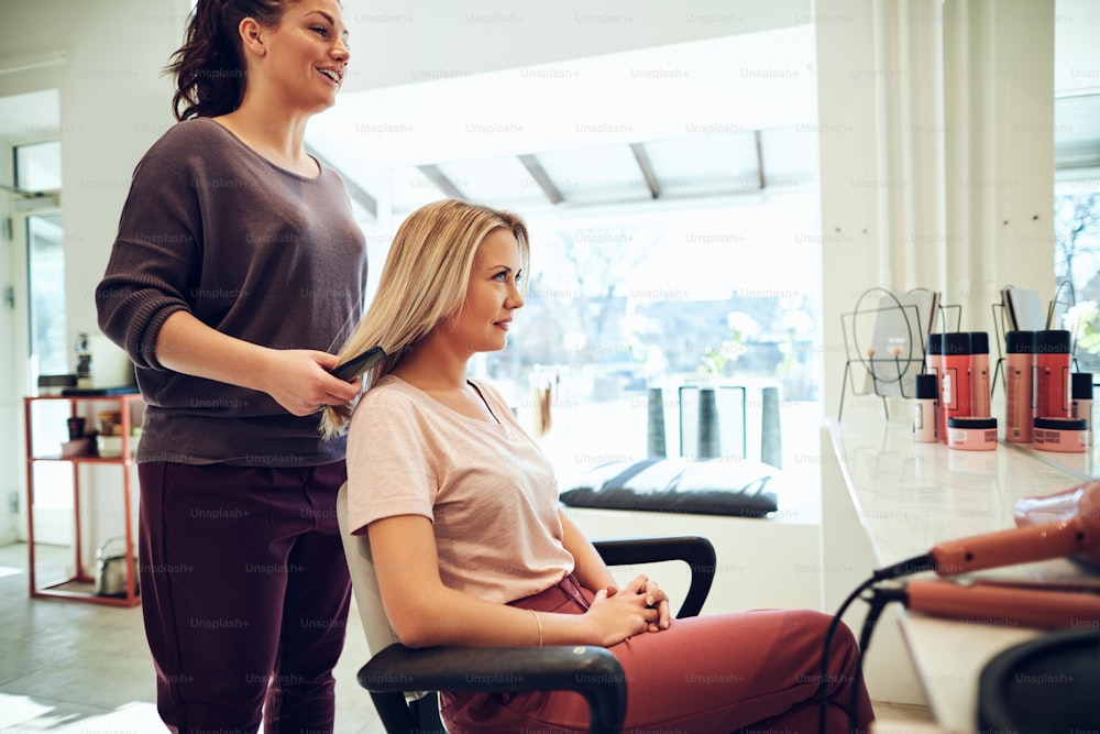 Young blonde woman smiling while sitting in a salon chair having her hair done during an appointment with her hairstylist