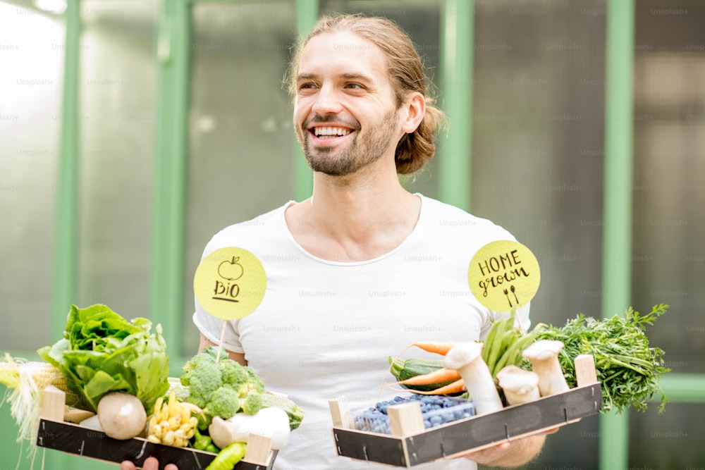 緑の壁の背景に新鮮な生野菜でいっぱいの箱を持つハンサムな男性のポートレート