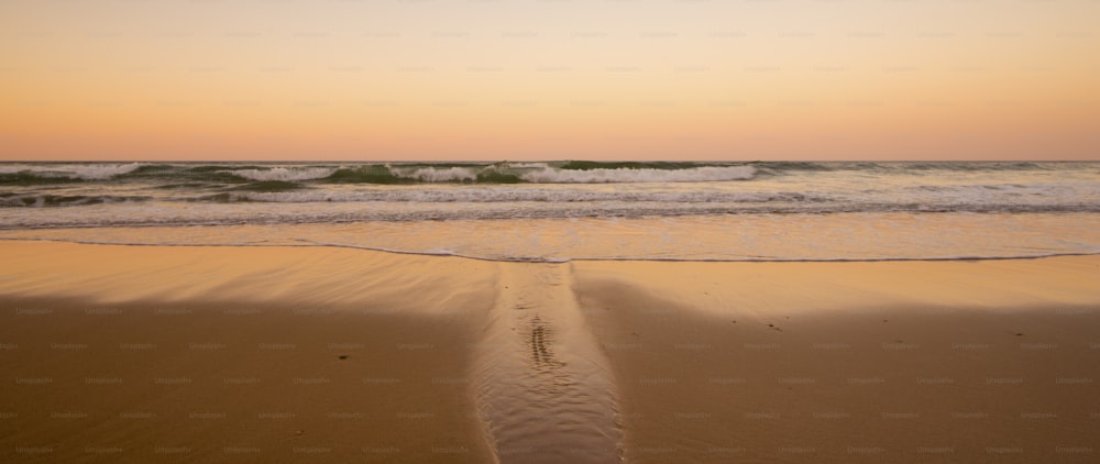 Schöner Sandstrand wie himmlischer Ort für Urlaub Sommerurlaub. Ozeanseite und Wellen während eines farbenfrohen Sonnenuntergangs im Hintergrund. Niemand da