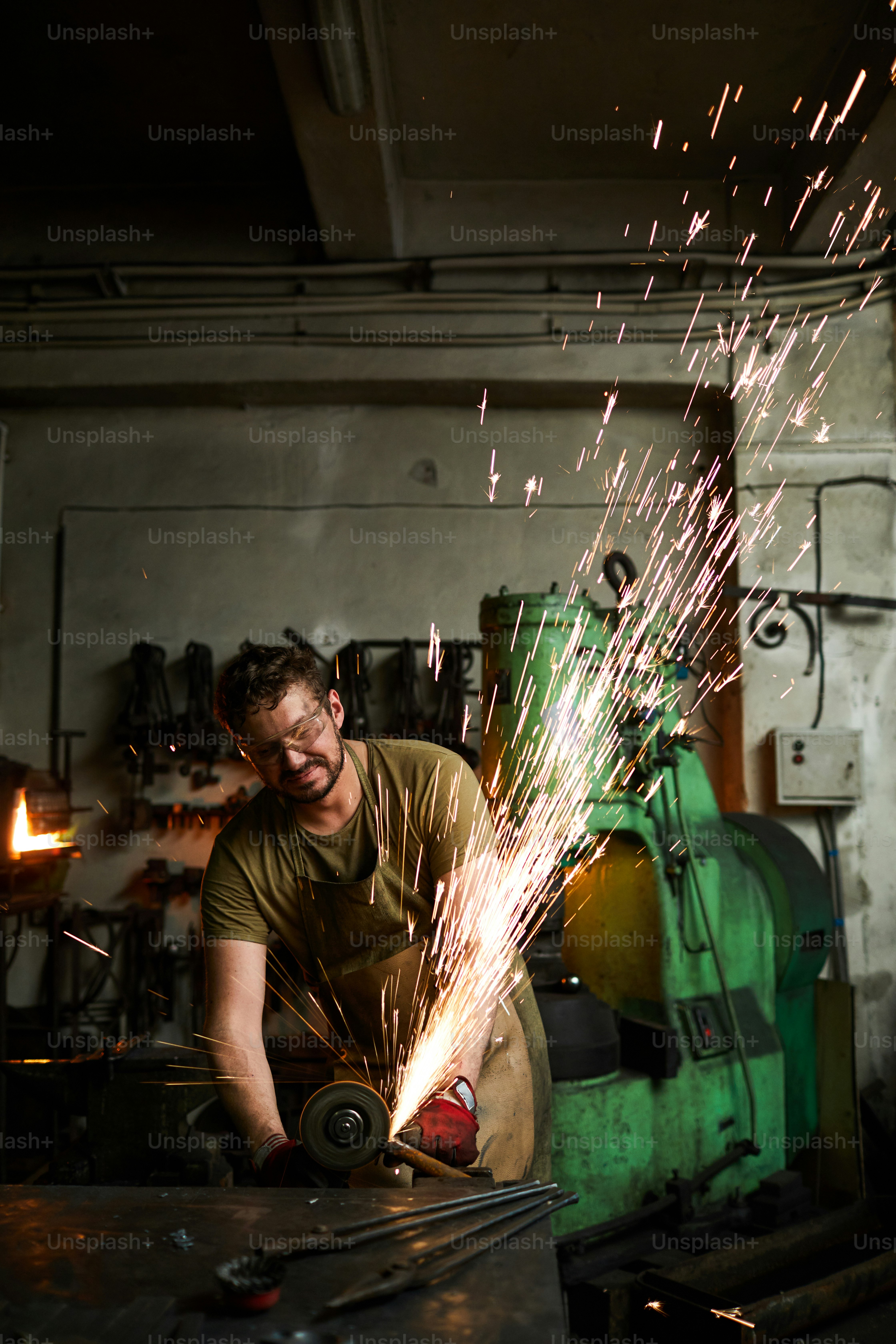 Young contemporary blacksmith standing by iron anvil and processing