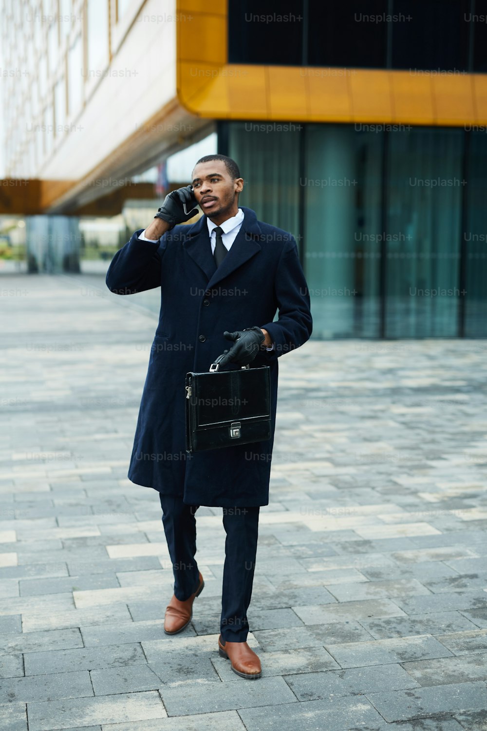 Junger afroamerikanischer Geschäftsmann ruft Kollegen oder Kunden an, während er sich im Freien bewegt