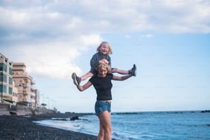 happy woman mother walk with his male son long hair blonde walking at the beach carrying him on the back. beautiful people enjoying lifestyle and life outdoor with the nature. vacation and lifestyle concept