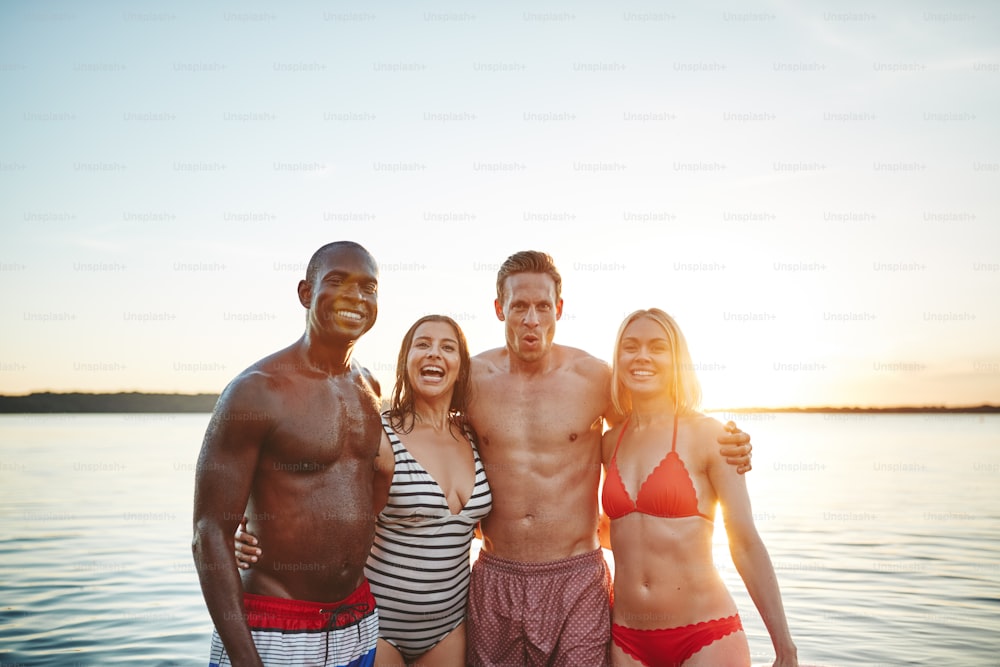 Diverse group of a smiling young friends in swimwear standing arm in arm together in a lake on a late summer afternoon