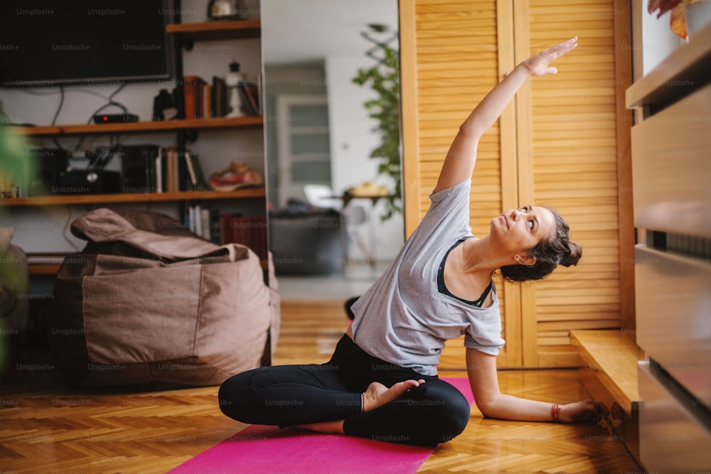 Femme faisant des exercices de yoga assise sur un tapis. En arrière-plan sacs paresseux, intérieur de la maison.
