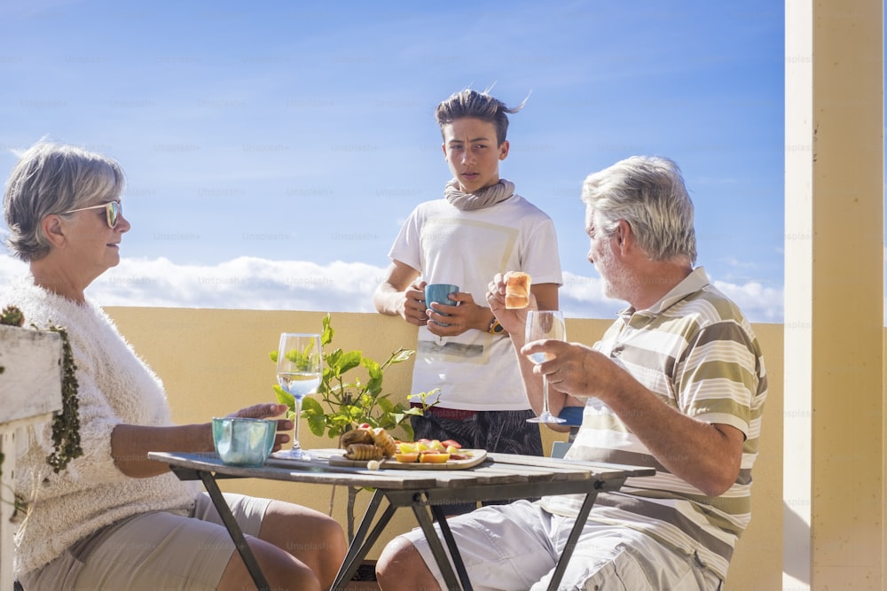 grandfathers adult mature and teenager grandson enjoy outdoor in the terrace some leisure with food and drinks. ocean and city view, vacation sunny day nice weather concept and background. happy people family together
