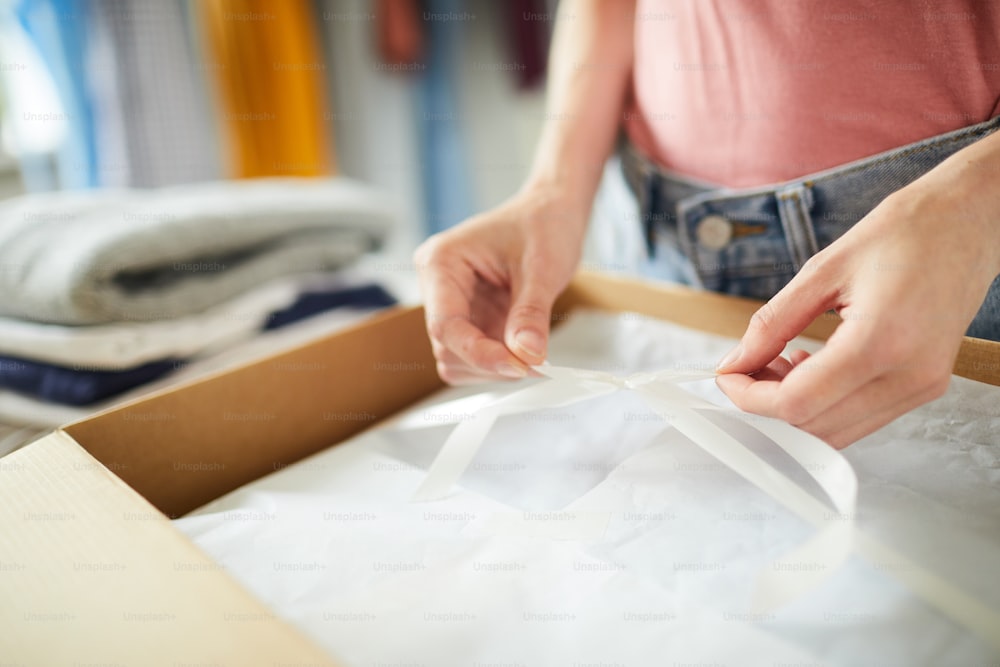 Contemporary designer tying up white ribbon over packed and folded clothes in box