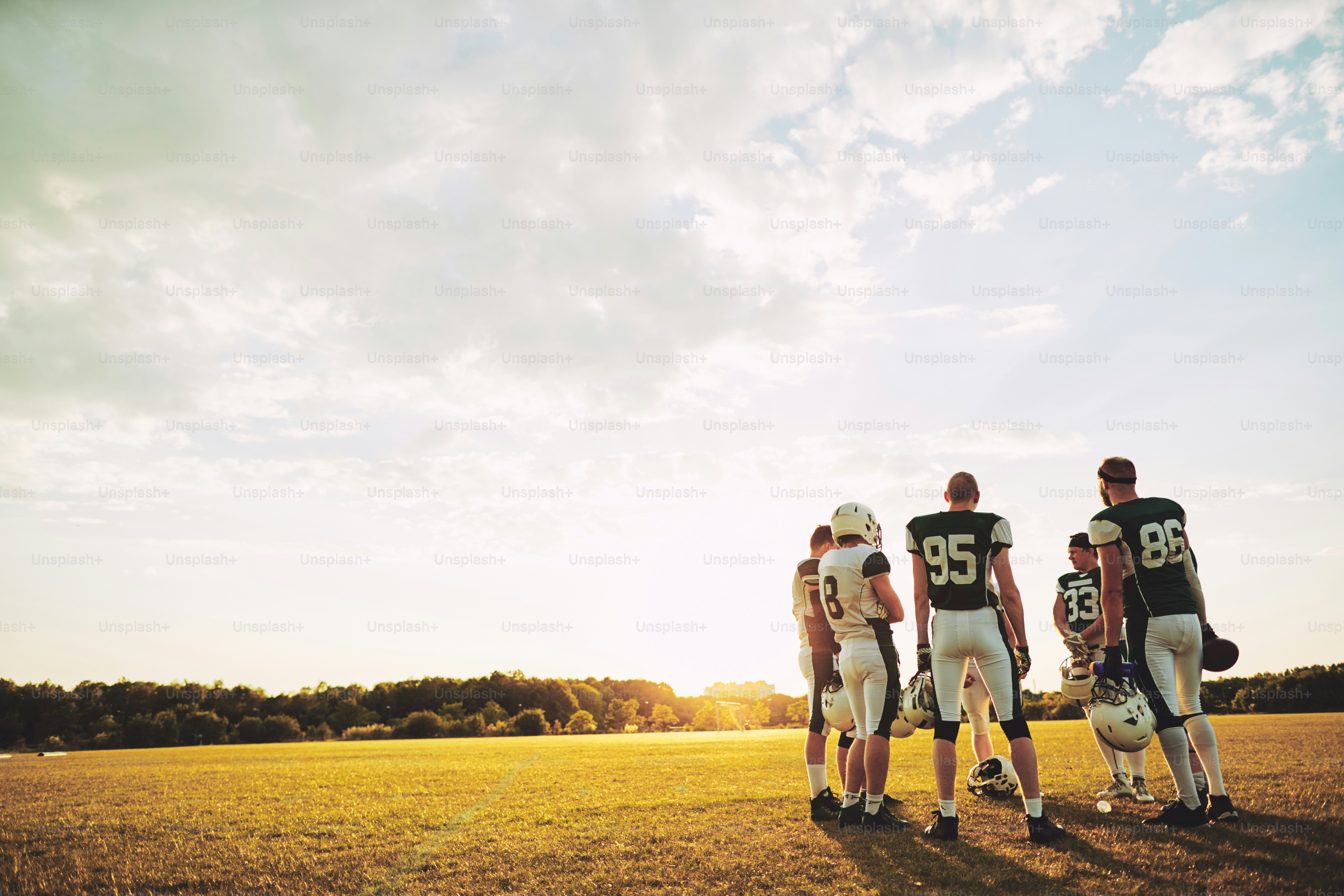 Gruppe junger American-Football-Spieler, die am Nachmittag gemeinsam auf einem Sportplatz stehen und während des Trainings über Strategie diskutieren