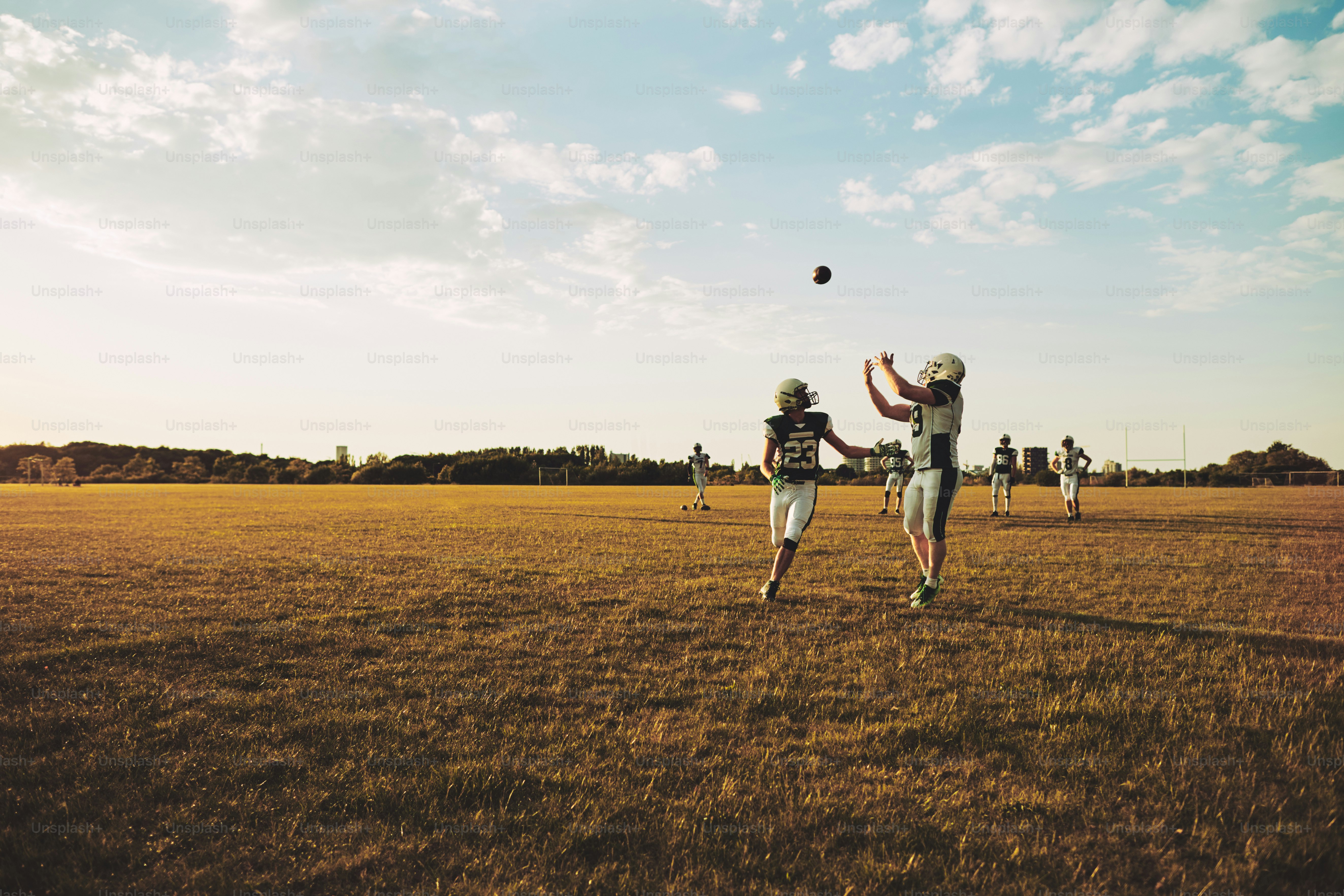 American-Football-Spieler rennt, um einen Pass während der Mannschaftsübungen auf einem Fußballfeld am Nachmittag zu fangen
