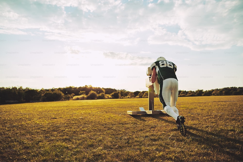 Jogador de futebol americano fazendo exercícios de tackle com um trenó de tackle do lado de fora em um campo esportivo durante um treino à tarde