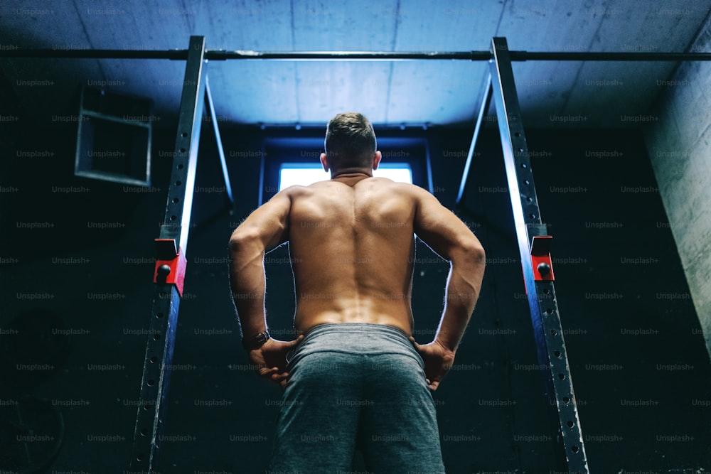 Shirtless Caucasian sporty man preparing to do chin-ups while standing in gym gym.