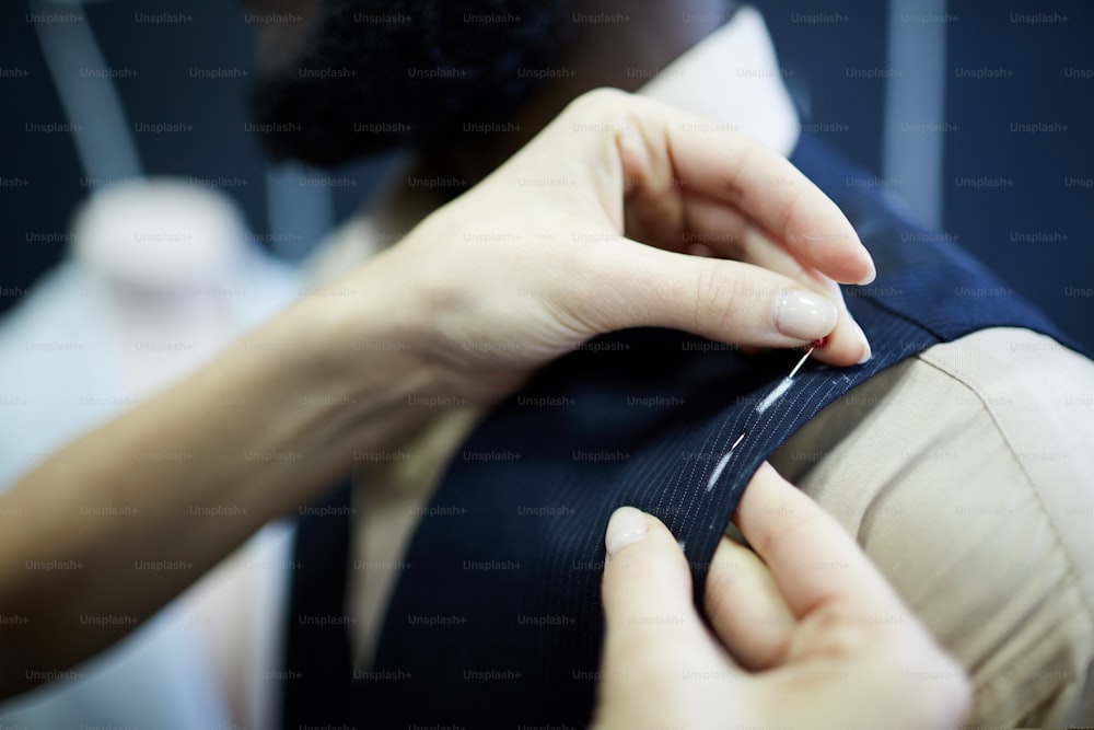 Close-up de alfaiate irreconhecível usando pinos de costura para fixar tecido enquanto corrige o colete durante o encaixe