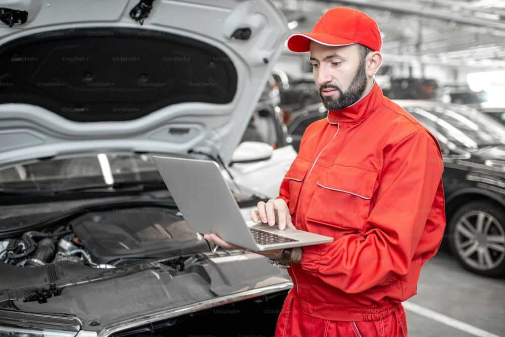 Two auto mechanics in red uniform doing engine diagnostics with computer in the car service