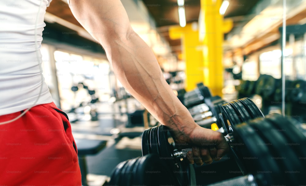 Close up of man picking dumbbell while standing in the gym.
