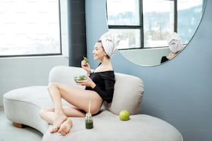 Beautiful woman eating healthy green food, relaxing after the spa procedures on the couch at home. Healthy lifestyle and self-care concept