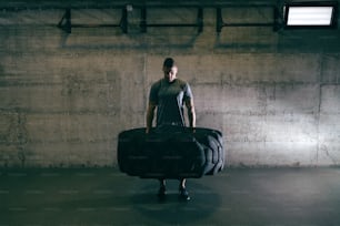 Caucasian muscular man lifting tire on his gym training. Destroy what destroys you.