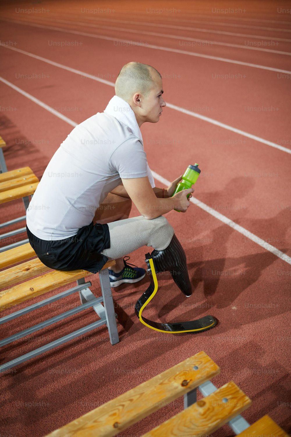 Sportif paralympique avec une bouteille d’eau en plastique assis sur un banc près de l’hippodrome et profitant d’une pause