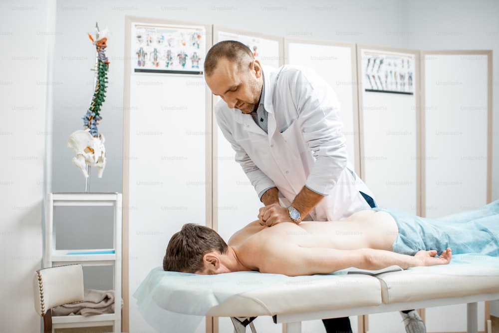 Professional senior physiotherapist doing manual treatment to a men's thoracic spine in the cabinet of rehabilitation clinic