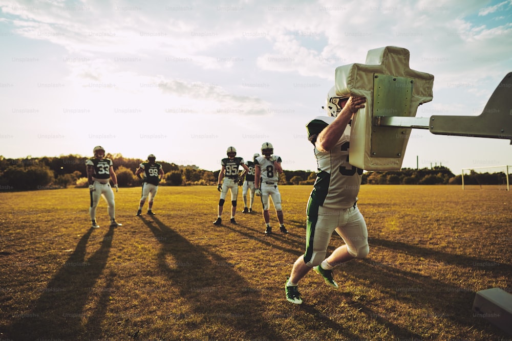 Team junger American-Football-Spieler, die während einer gemeinsamen Trainingseinheit auf einem Sportplatz Schlitten in Angriff nehmen