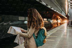 Giovane viaggiatore della ragazza riccia della testa rossa della giovane donna con lo zaino e la mappa nella stazione della metropolitana di fronte al treno