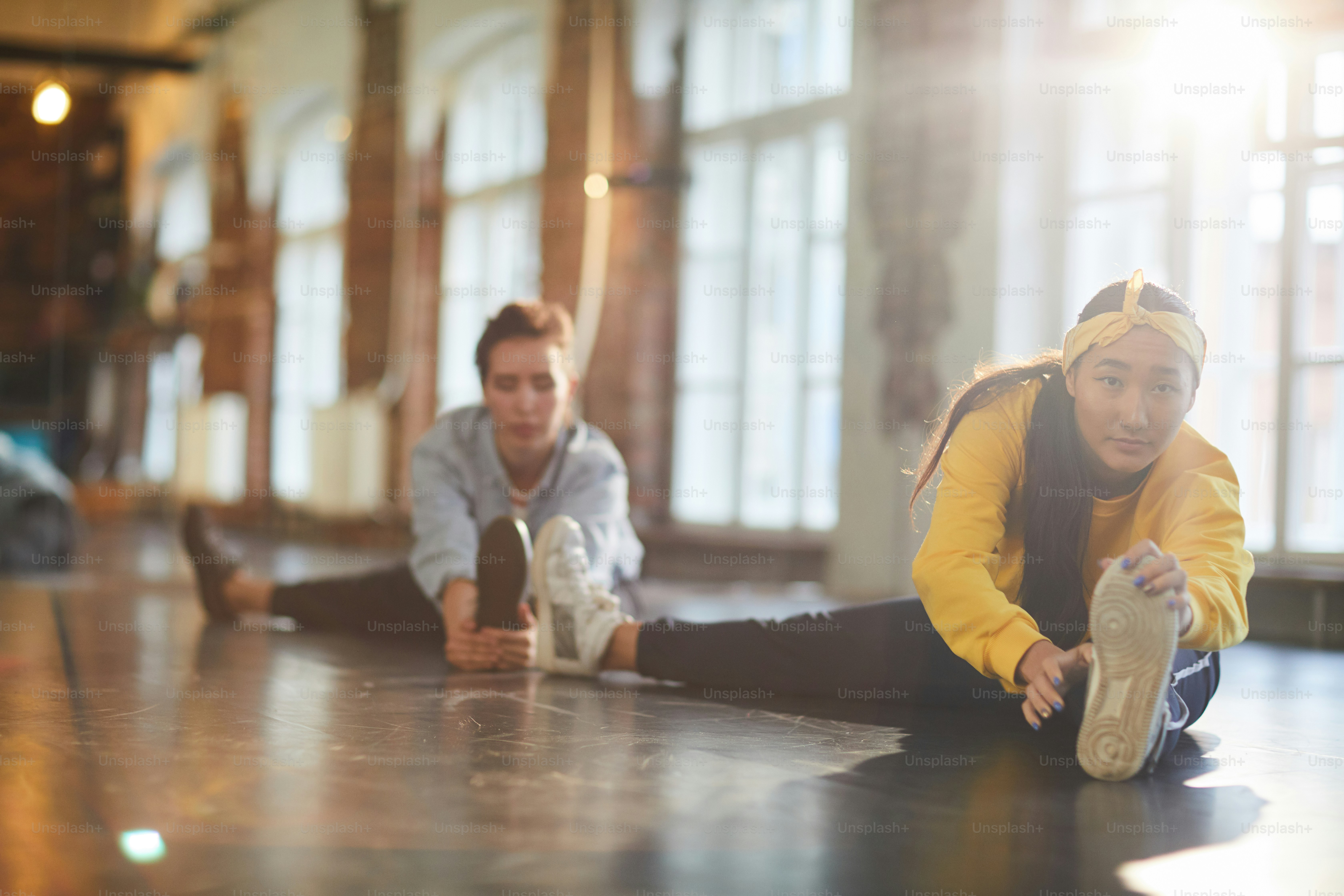 Two young women in activewear doing stretching exercise for legs on the floor of studio
