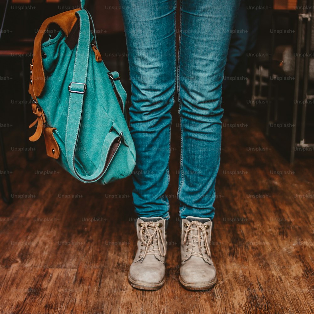 Crop photo of young woman feet girl traveler in jeans and boots with backpack indoors