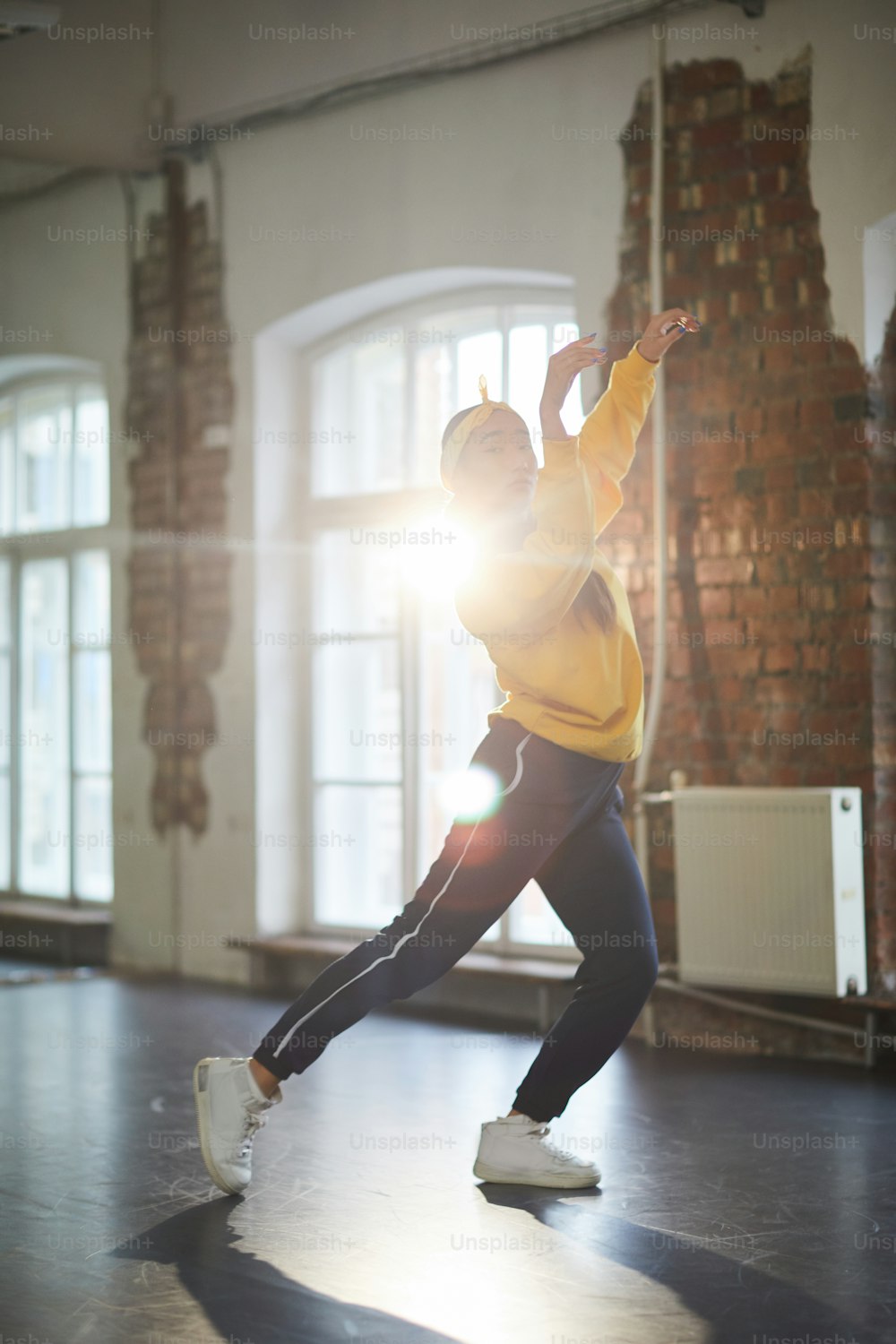 Active girl in sweatshirt, sweatpants and cross-shoes performing breakdance in studio