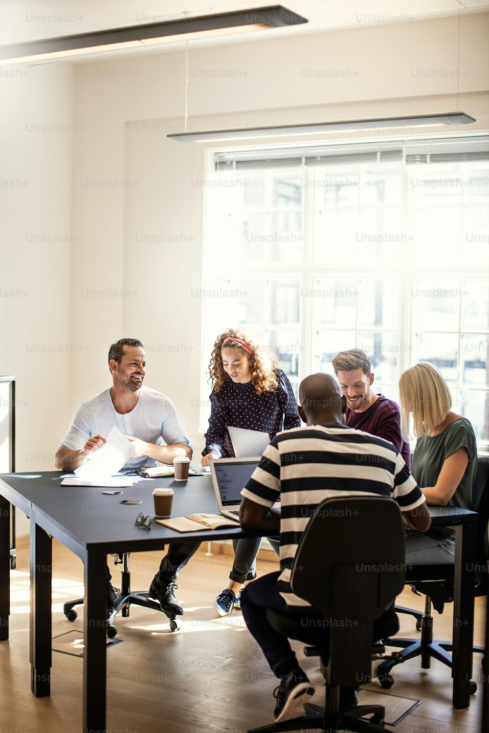 Un grupo diverso de jóvenes diseñadores sonrientes que trabajan juntos alrededor de una mesa de la sala de juntas en una oficina