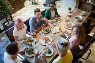 Several young friendly men and women gathered by table served with food for dinner and talk