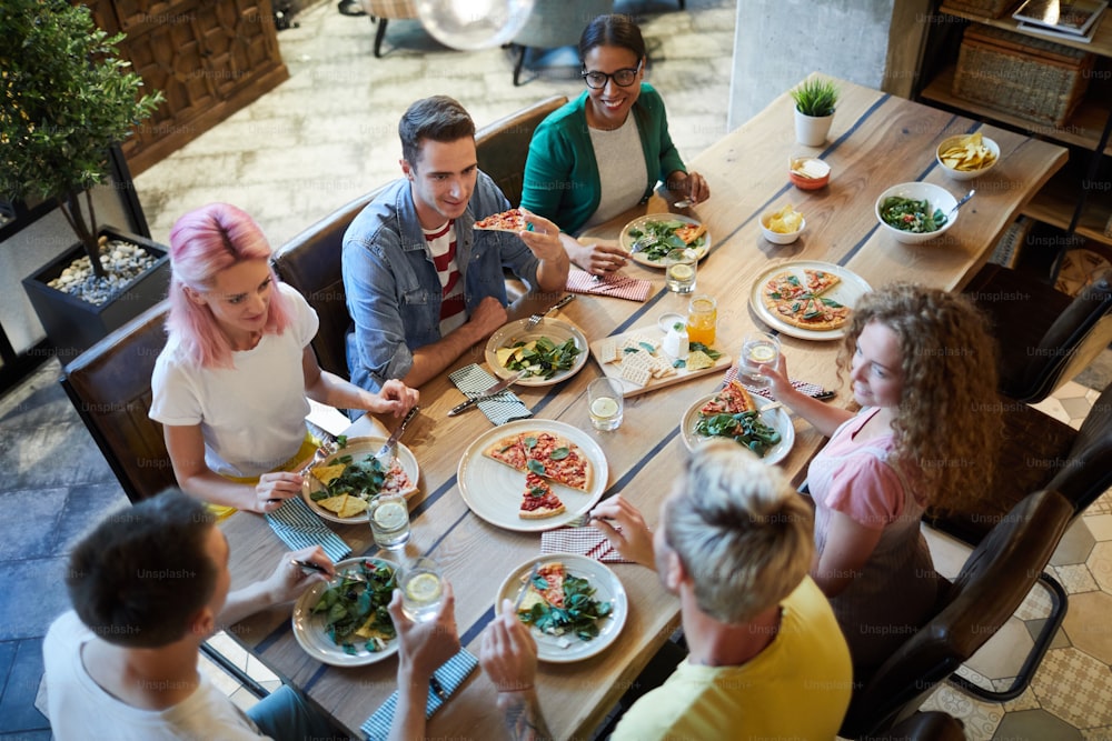 Several young friendly men and women gathered by table served with food for dinner and talk