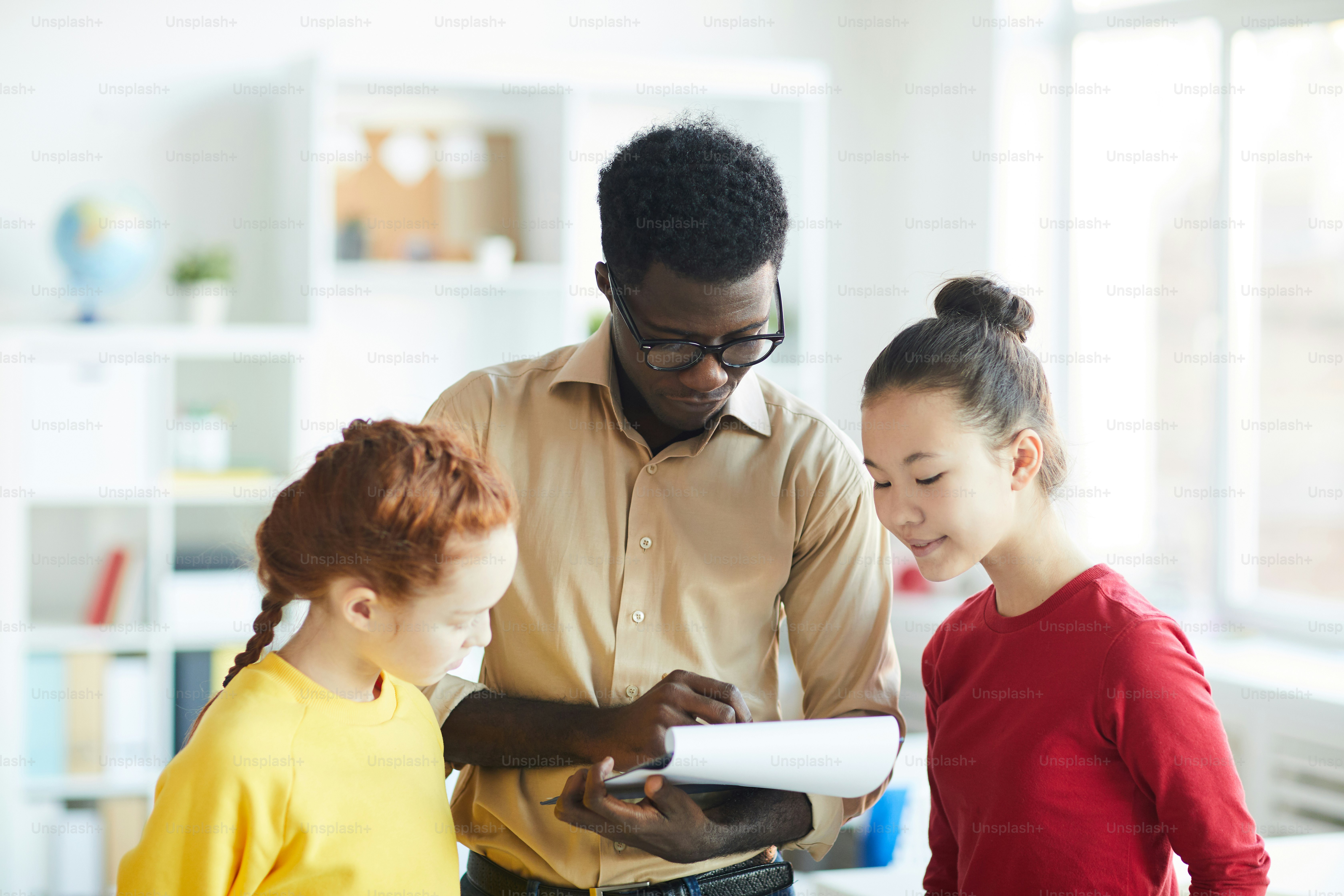 Maestro de escuela afroamericano mostrando y discutiendo las calificaciones con sus dos alumnos después de la clase