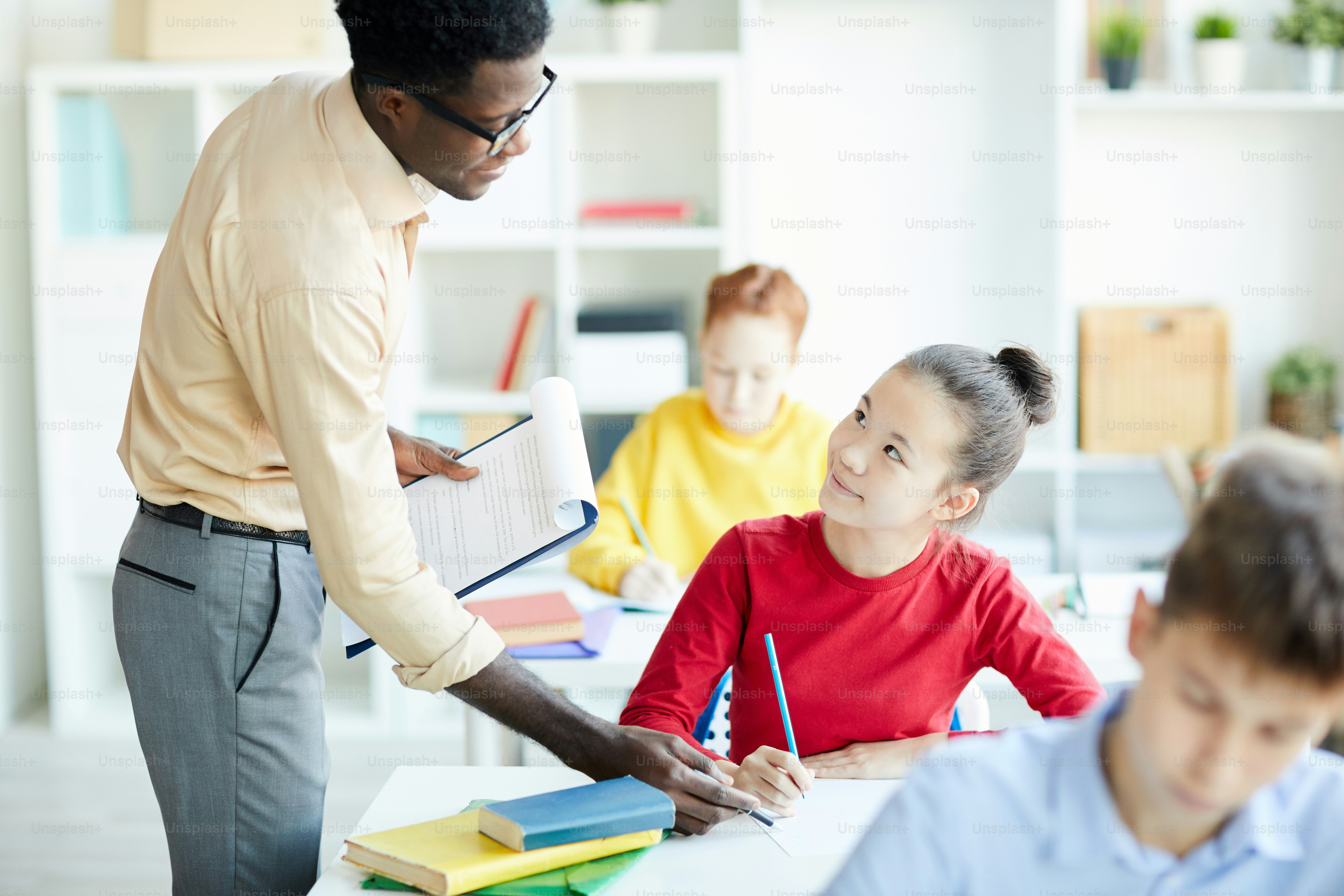 Colegiala bonita con lápiz escuchando la explicación del profesor de algunas notas en su cuaderno en la lección
