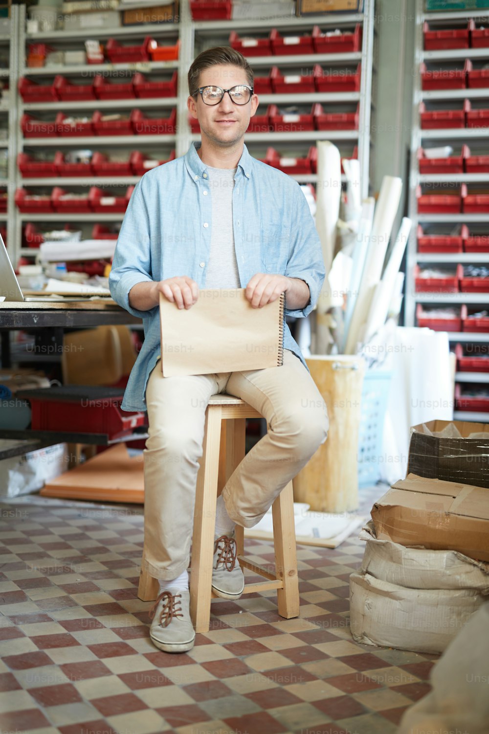 Young master of artwork with notepad sitting on wooden stool inside his workshop