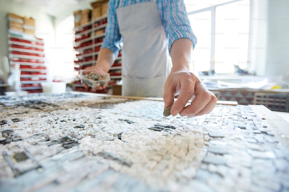 Close up shot of unrecognizable artist laying out tiles while creating mosaic in workshop, copy space