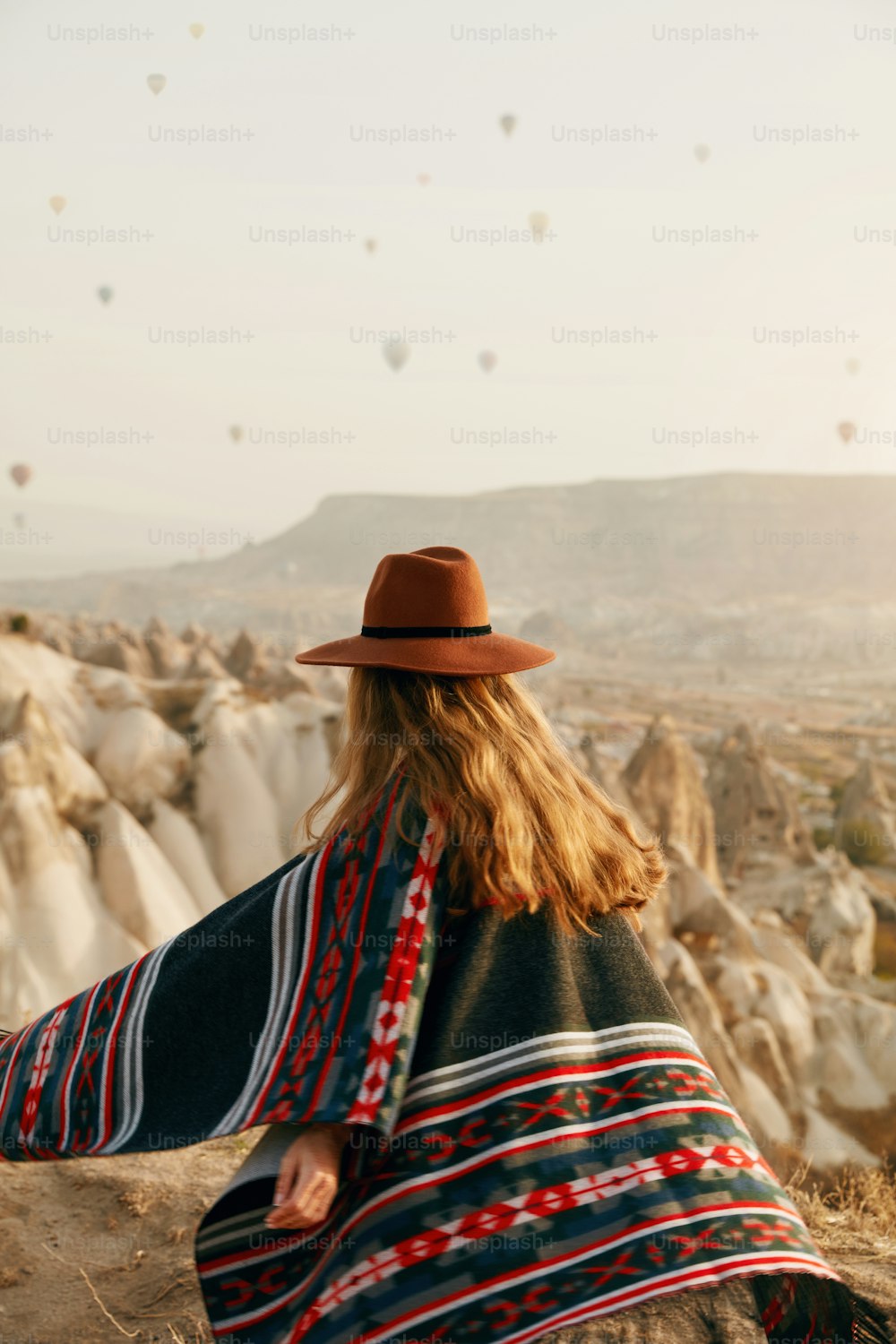 Viajar. Mujer con sombrero divirtiéndose al aire libre, disfrutando del paisaje con globos aerostáticos en el cielo. Alta resolución