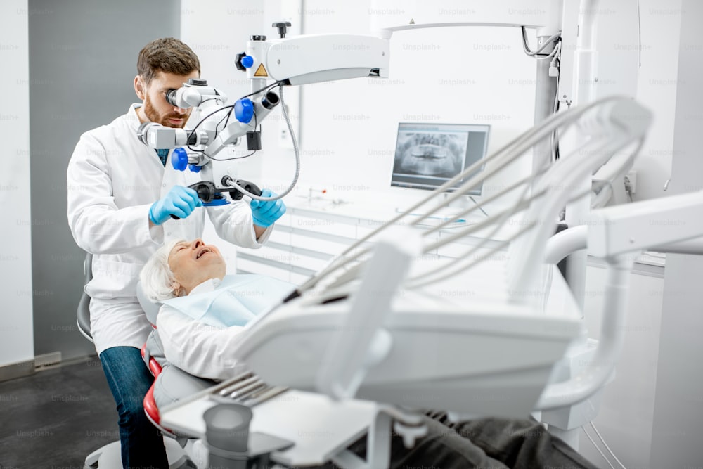 外科歯科医院でプロの顕微鏡で歯を見ている年配の女性を調べる男性歯科医