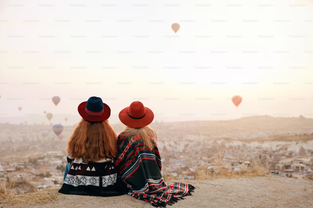 Le persone viaggiano. Donne in cappelli seduti sulla collina che godono di vista volanti mongolfiere in Cappadocia Turchia. Alta risoluzione