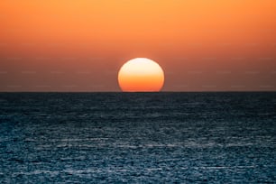 Momento do pôr do sol ou nascer do sol sobre o oceano com o sol tocando a linha do horizonte na água - conceito romântico e turístico para viagens de férias colorido