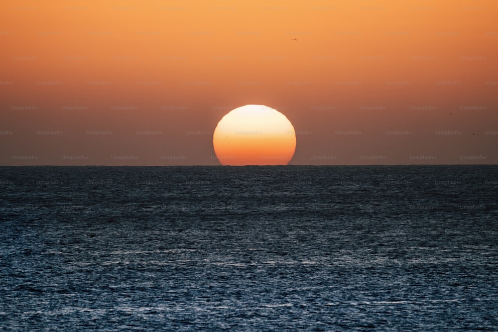 Sonnenuntergang oder Sonnenaufgang über dem Ozean mit Sonne, die die Horizontlinie auf dem Wasser berührt - romantisches und touristisches Konzept für den Reiseurlaub Hintergrund farbig