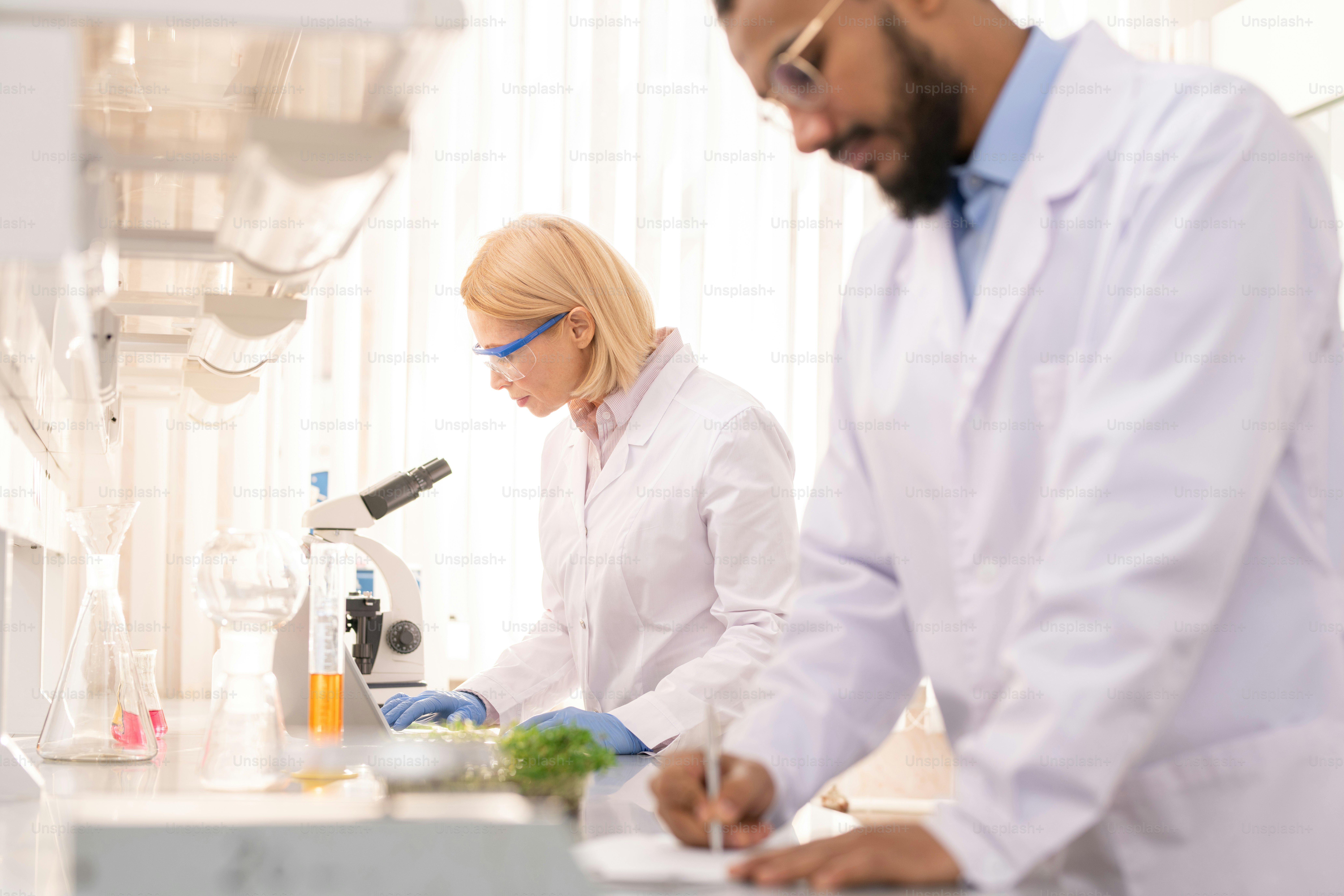 Serious concentrated mature lady scientist in protective eyewear standing at table and preparing for experiment while working in research laboratory