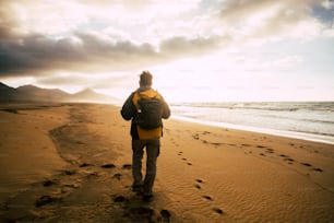 People in back view walking alone with his backpack on the desolation beautiful wild beach for alternative concept of tourism vacation - adventure and explore scenic place - freedom and feeling the nature lifestyle