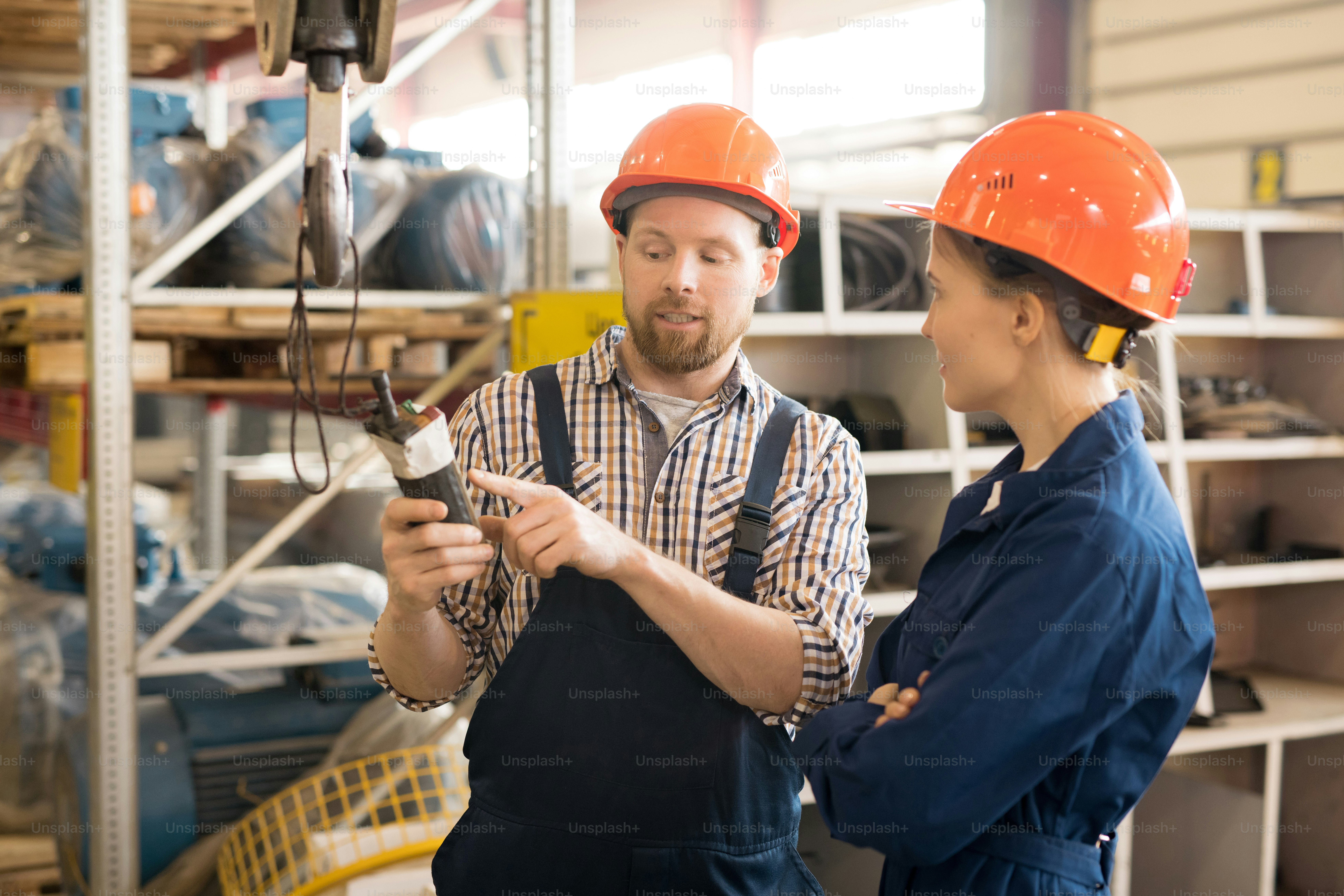 Confident engineer showing part of new equipment to his colleague or trainee while describing its purpose