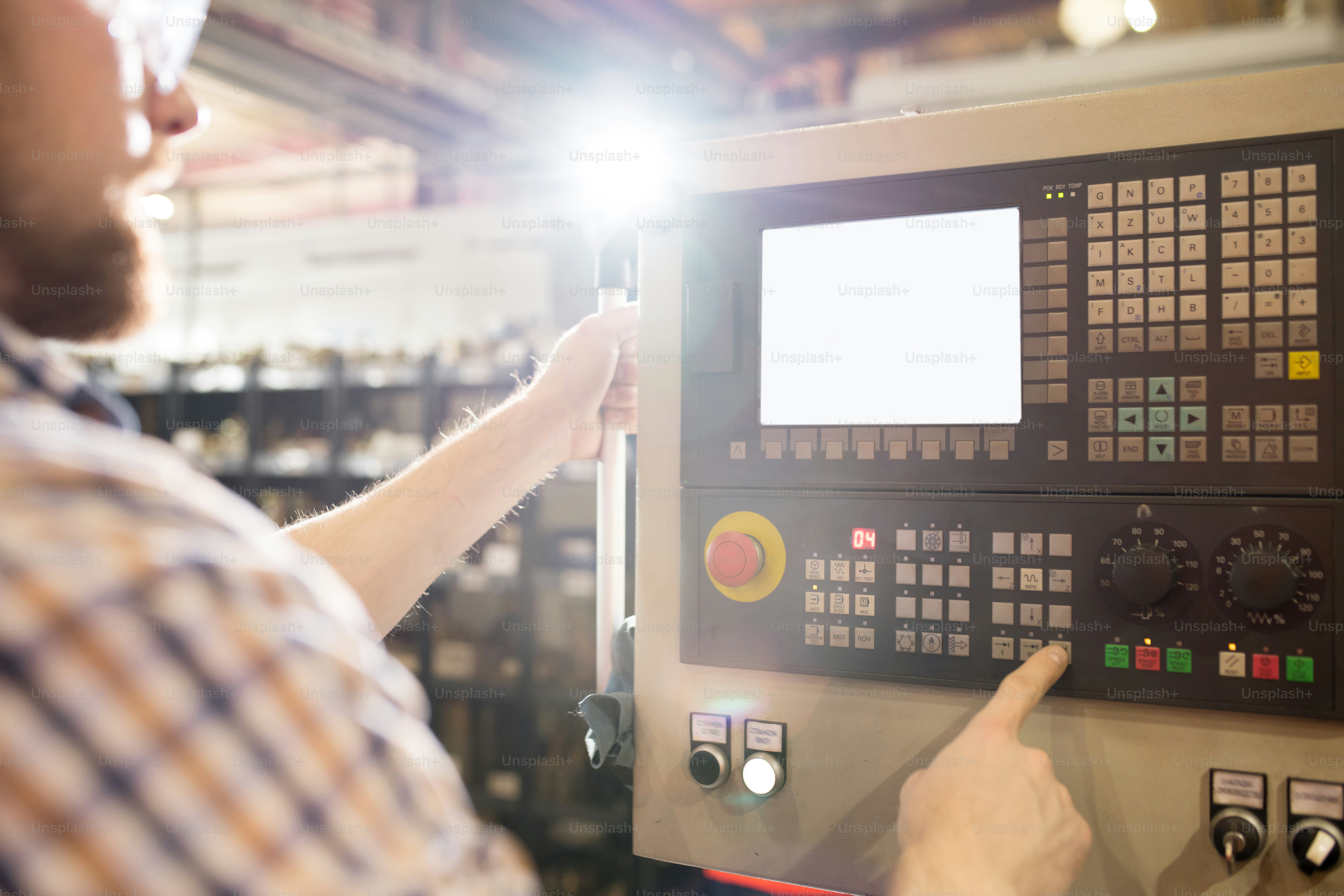 Junger Ingenieur oder Techniker, der eine der Tasten auf dem Bedienfeld drückt, während er neben der Industriemaschine steht