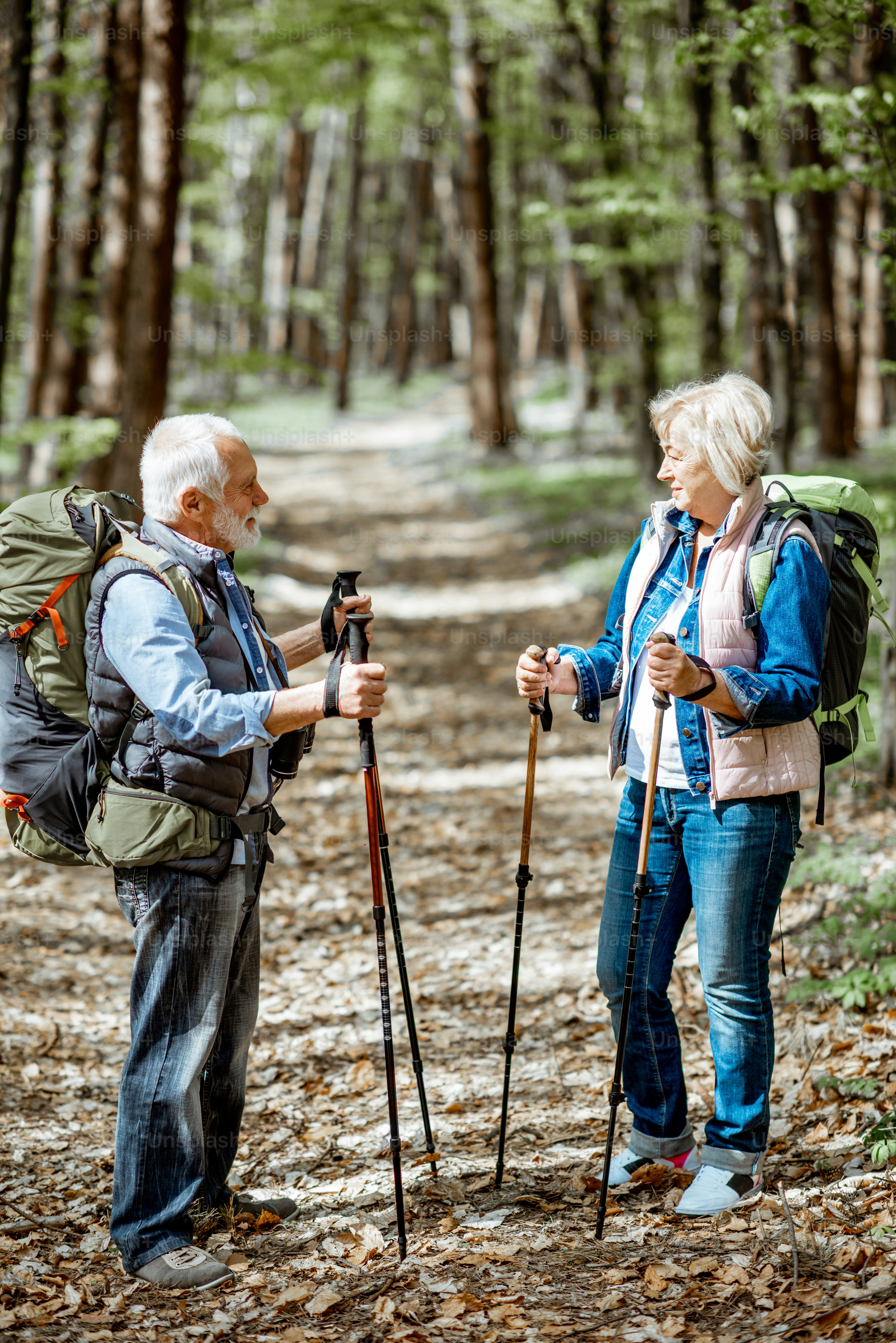 Schönes älteres Paar, das mit Rucksäcken und Trekkingstöcken im Wald wandert. Konzept des aktiven Lebensstils im Ruhestand