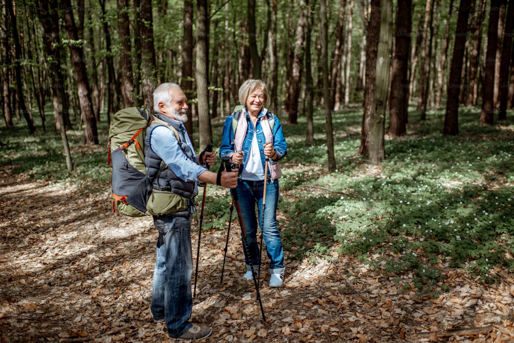 Schönes älteres Paar, das mit Rucksäcken und Trekkingstöcken im Wald wandert. Konzept des aktiven Lebensstils im Ruhestand