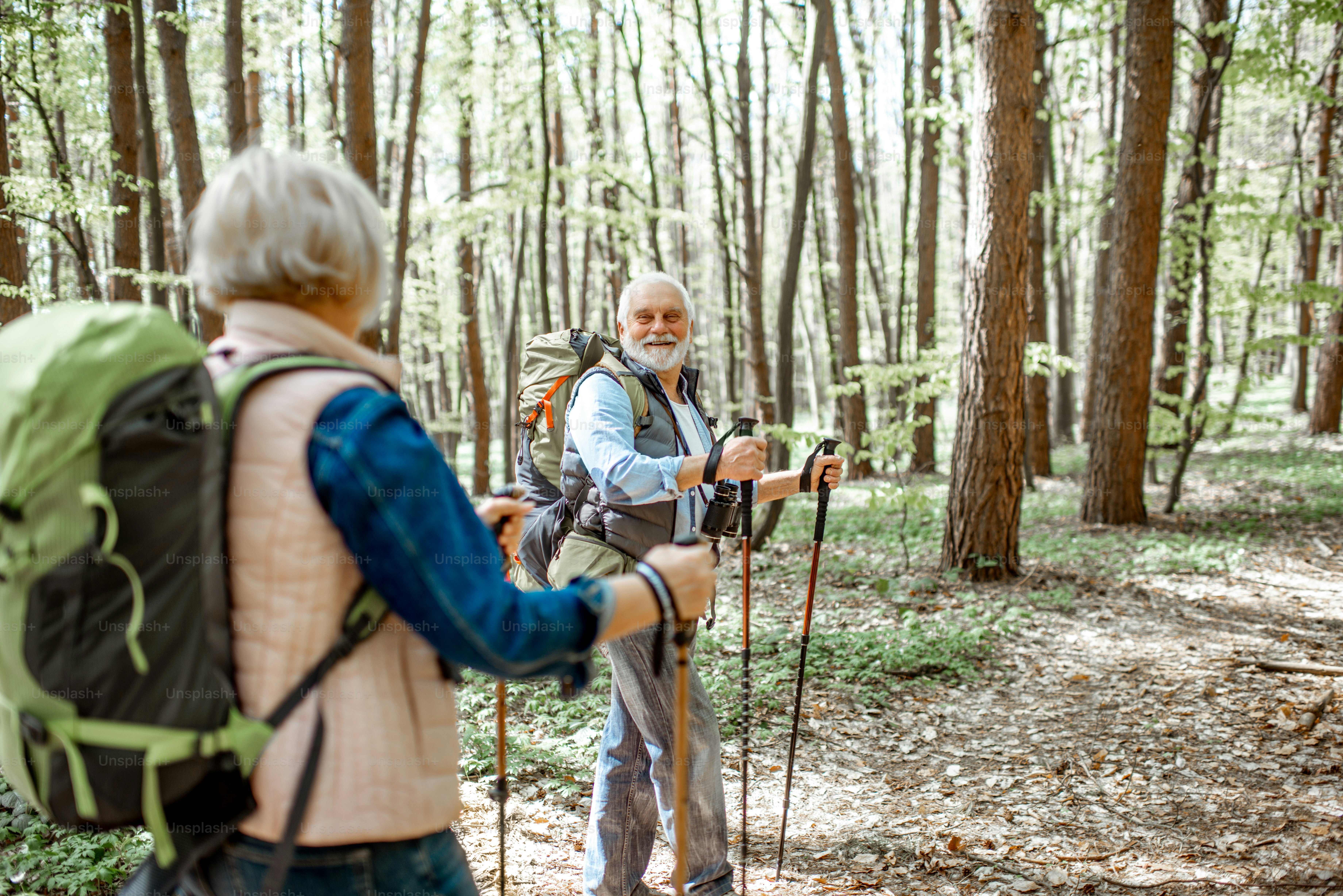 Schönes älteres Paar, das mit Rucksäcken und Trekkingstöcken im Wald wandert. Konzept des aktiven Lebensstils im Ruhestand