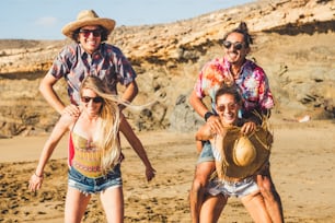 Gruppo pazzo di persone amici caucasici uomini e donne che giocano insieme in spiaggia in vacanza - gli uomini saltano sulla schiena della donna che deve portarli - tutti ridono molto e si divertono