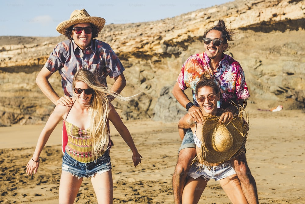 Verrückte Gruppe von Menschen kaukasische Freunde Männer und Frauen spielen zusammen am Strand im Urlaub - Männer springen auf den Rücken der Frau, die sie tragen muss - alle lachen viel und haben Spaß