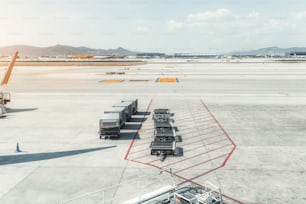 Vista de la maquinaria en la zona de embarque de una terminal contemporánea del aeropuerto El Prat en Barcelona, con cuatro contenedores con una comida y carros de equipaje conectados vacíos, campo de despegue al fondo