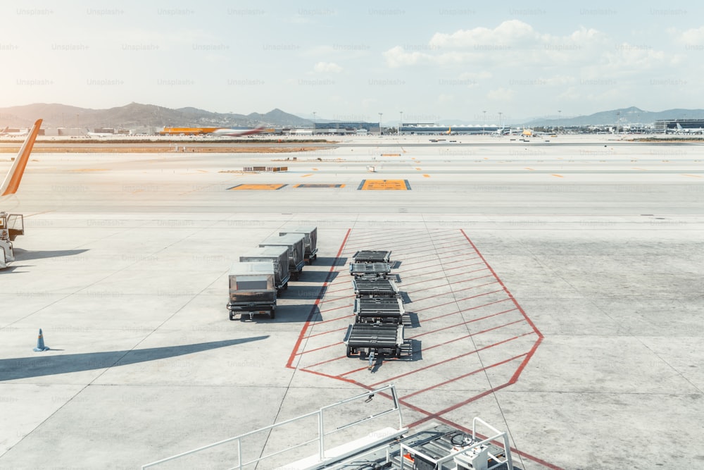 View of machinery on the boarding area of a contemporary airport terminal El Prat in Barcelona, with four containers with a meal and empty connected baggage carts, take-off field in the background
