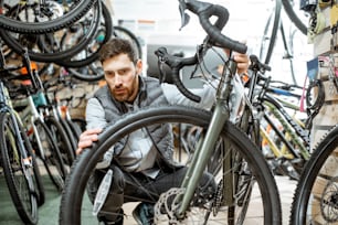 Hombre que elige una bicicleta nueva para comprar de pie en la tienda con muchas bicicletas y equipos deportivos en el interior
